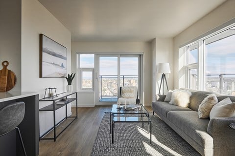 a living room with a gray couch and a glass coffee table and a large window